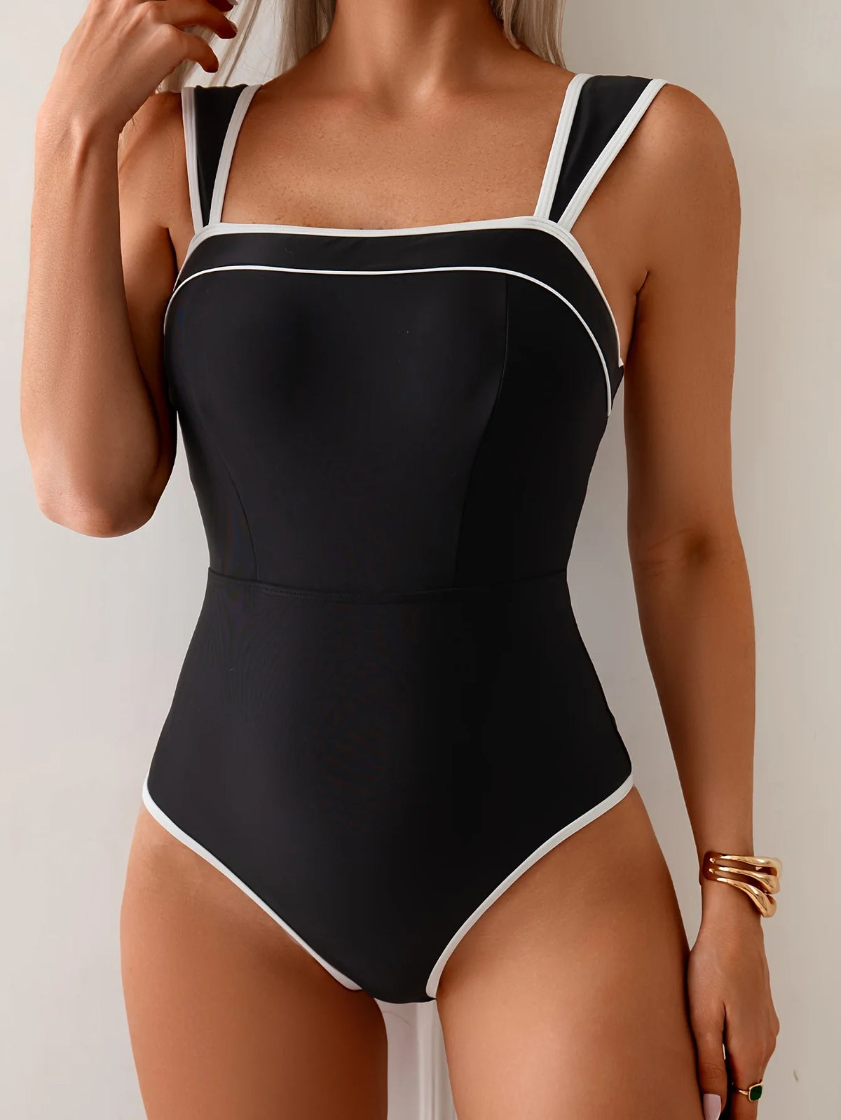 Black one-piece swimsuit with a square neckline, wide straps and white contrast trim