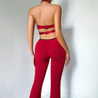 Back of the burgundy catsuit with the halter neck, a bare back crossed by one clasp strap, and flared legs