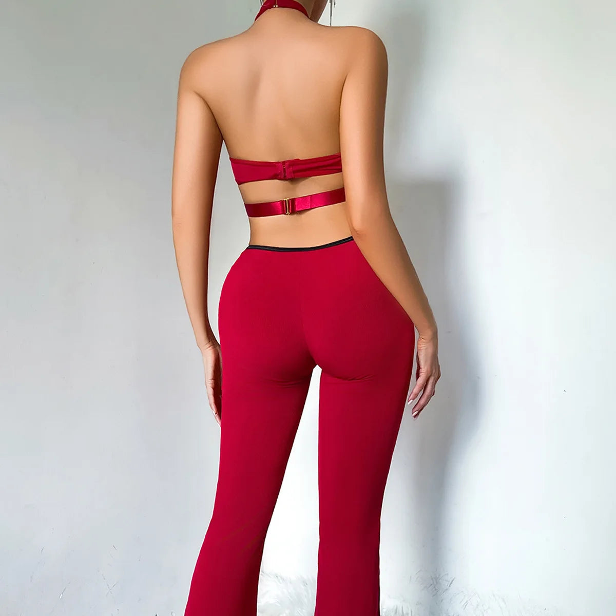 Back of the burgundy catsuit with the halter neck, a bare back crossed by one clasp strap, and flared legs